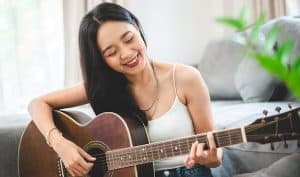 Woman playing sustainable, eco-conscious acoustic guitar in home.